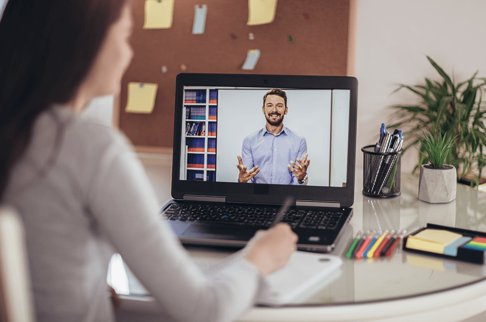 Woman at desk taking notes while watching online conference