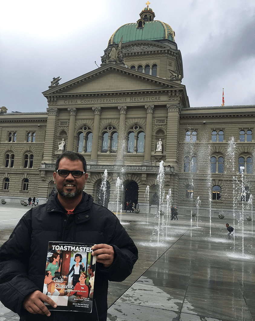 Akbar Khan, ACS, ALB, of Goa, India, smiles in front of the Federal Palace of Switzerland parliament building while on vacation in Bern, Switzerland.