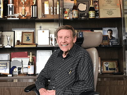 Toastmaster Burt Epstein sits in chair with awards in background