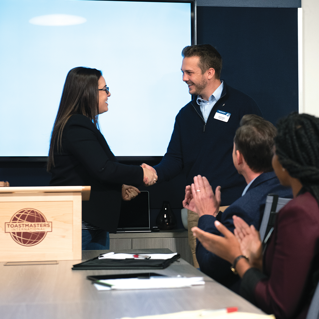 Woman at lectern shakes hands with man