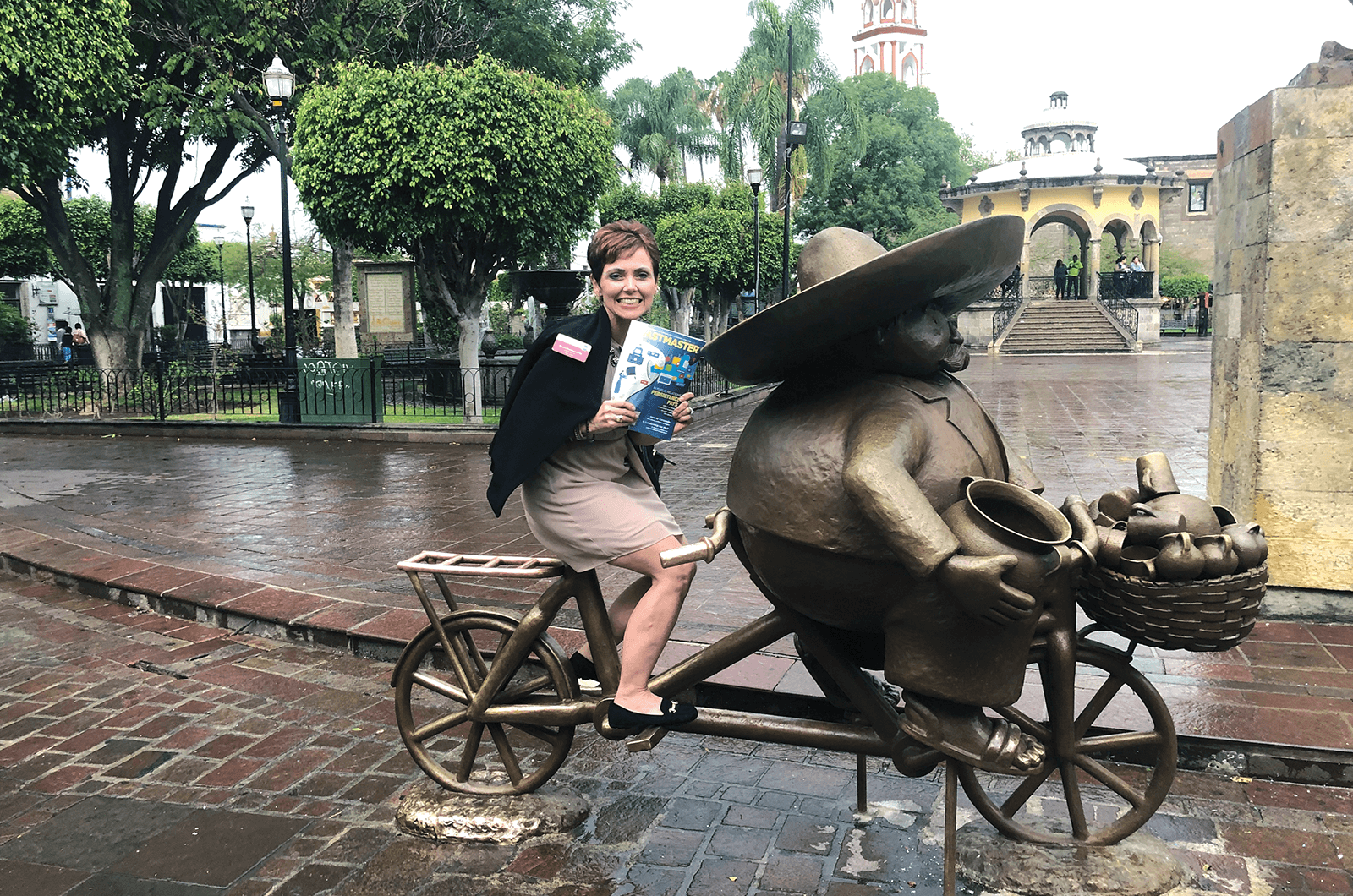 Maria Martinez, DTM, of Lakeland, Florida, poses on a statue of a peddler on a bicycle in Guadalajara, Mexico.