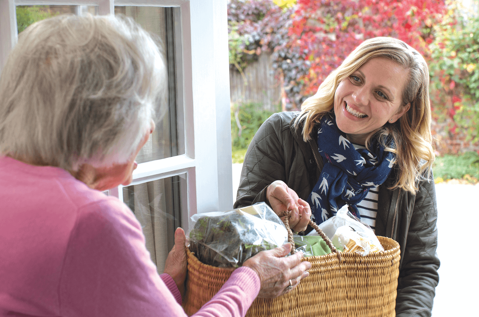 Younger woman hands older woman a basket of food