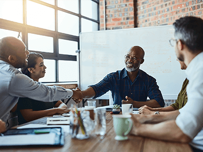 Man sitting at head of table shaking hands with employee