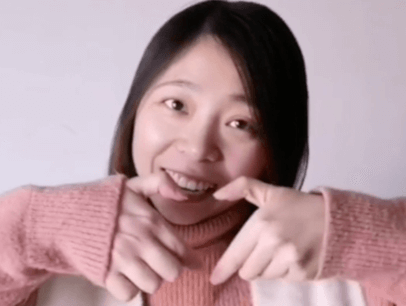 Woman in pink sweater smiling while holding up hands making a heart shape