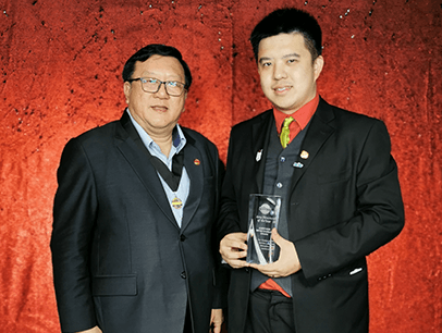 Men in black suits with red backdrop holding trophy onstage