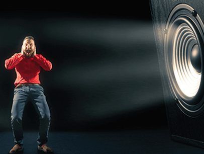 Man in red shirt holding hands over ears with speaker on side of him