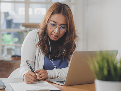 Woman taking notes while watching laptop